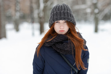 Closeup beautiful winter portrait of young adorable serious redhead woman in cute knitted hat winter snowy park