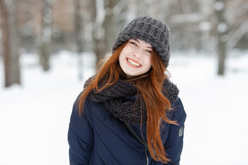 Closeup beautiful winter portrait of young adorable smiling redhead woman in cute knitted hat winter snowy park