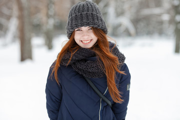Closeup beautiful winter portrait of young adorable smiling redhead woman in cute knitted hat winter snowy park