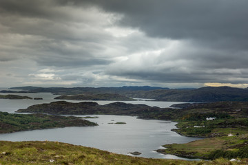 Fototapeta na wymiar Assynt Peninsula, Scotland - June 7, 2012: Under dark cloudy sky aerial view on Loch Ardhair with intrusion of the ocean in the wild landscape of hills, mountains, bare land, small and larger islands.