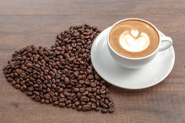 Coffee cup of latte art with coffee beans in heart shape on wood