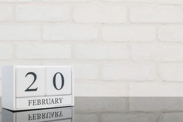 Closeup white wooden calendar with black 20 february word on black glass table and white brick wall textured background with copy space in selective focus at the calendar