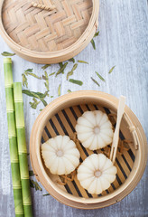 Lychee mochi - Japanese mini dessert cake in a bamboo steamer basket, Bamboo straws are next to the bamboo steamer. green tea leaves scattered on the tabletop 