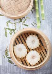 Lychee mochi - Japanese mini dessert cake in a bamboo steamer basket, Bamboo straws are next to the bamboo steamer. green tea leaves scattered on the tabletop 