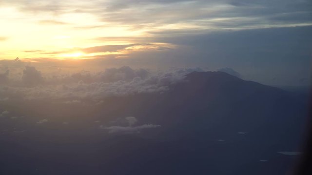 View through an airplane window on the volcano, mountains, sky and clouds. Rocky Mountains through Airplane Window. Aerial view Clouds and sky as seen through window of an aircraft. 4K video. Aerial