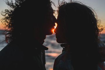 Young hipster couple with long curly hair kissing at sunset