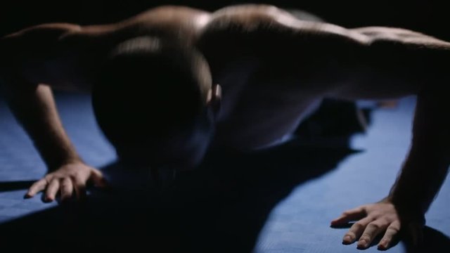 Shirtless man performing clap push-ups during training in dark gym