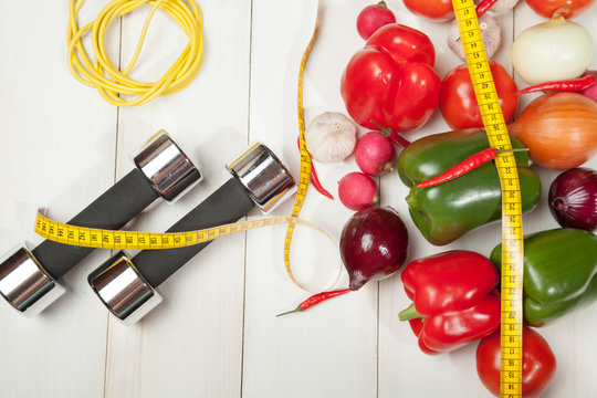 Sport and diet. Healthy lifestyle. Vegetables, dumbbells. Peppers, tomatoes, garlic, onions radishes on a white background