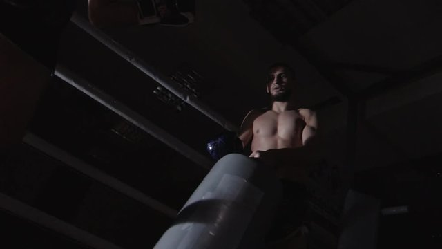 Low angle of muscular MMA instructor holding kicking pad while his partner practicing kicks on ring in slow motion and then they bumping fists in boxing gloves together