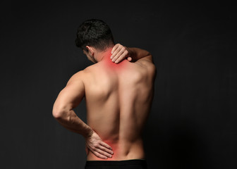 Fototapeta na wymiar Young man suffering from back pain on black background. Health care concept