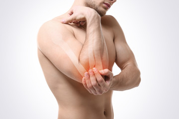 Young man suffering from elbow pain on light background. Health care concept