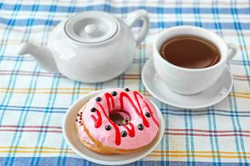 Delicious donuts with cup of tea on checkered tablecloth background