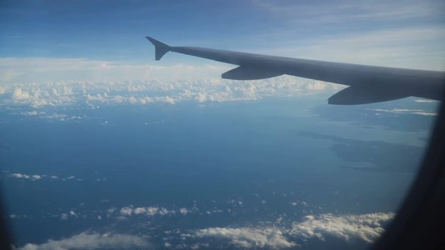 View through an airplane window on the tropical island, ocean, sky and clouds. Aerial view sea, clouds and sky as seen through window of an aircraft. 4K video. Aerial footage. Travel concept.