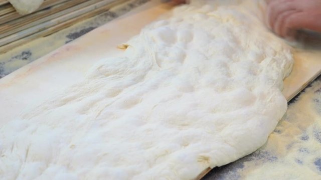 slowmotion of Baker stretching dough of a focaccia on a wooden cutting board