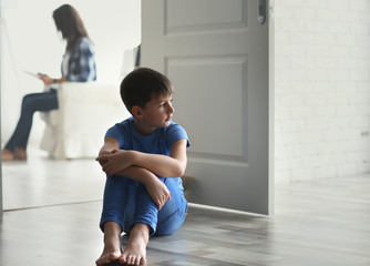 Sad little boy sitting on floor beside door