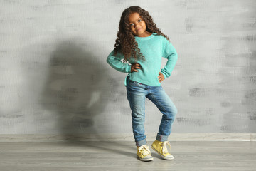 Cute little African American girl against grey wall. Fashion concept
