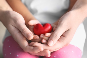 Child and adult person holding small red heart, closeup. Adoption concept