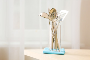 Set of metal kitchen utensils in glass with napkin on table