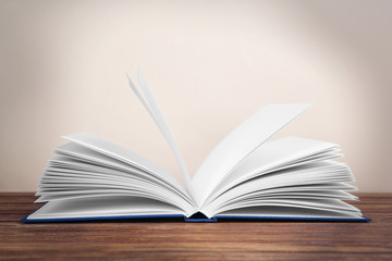 Opened book on wooden table and beige background