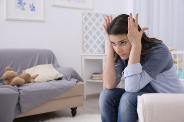 Depressed young woman sitting in armchair at home