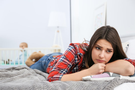 Depressed young woman lying on bed at home
