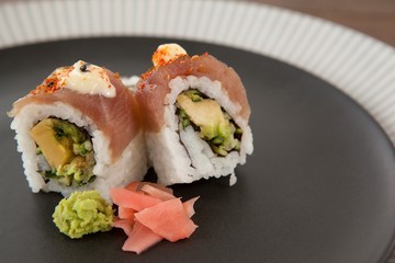 Two uramaki sushi served in black round plate on wooden table