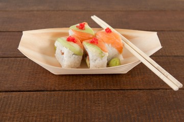 Four uramaki sushi served with chopsticks in wooden boat plate