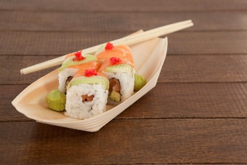 Four uramaki sushi served with chopsticks in wooden boat plate