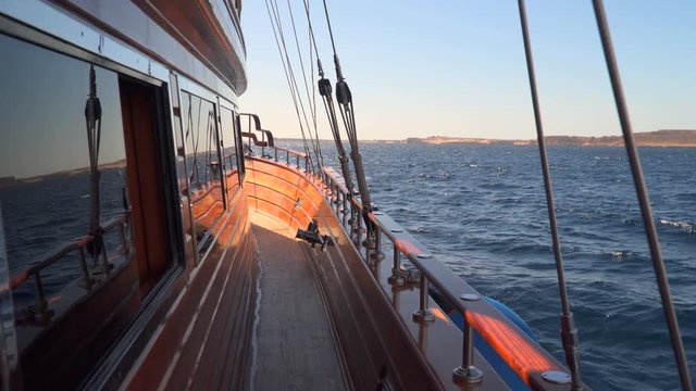 The deck of sailing yacht. View of the coast from the yacht. In the windows of staterooms reflected sea