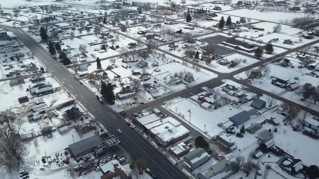 Aerial rural town center home business and traffic climb. Aerial point of view. Winter storm blizzard white snow. Rural farm community. Hard seasonal weather. Hazard to driving. Surveillance spy.