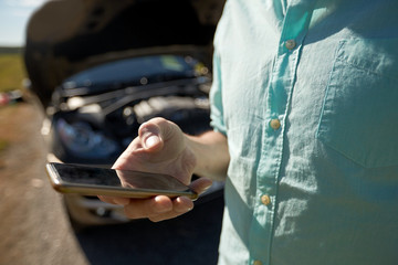 close up of man with smartphone and broken car