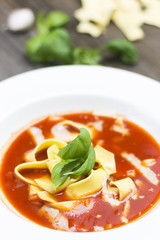 Red Tomato Soup with Yellow Wheat Noodles and fresh Basil Leaves. Raw ingredients on Wooden Background.