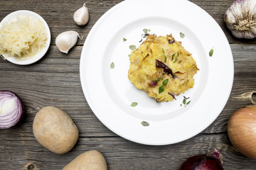 Cabbage and Potato Meal on White Plate with Raw Ingredients on Wooden Background