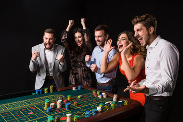 Group of young people behind roulette table on black background