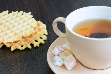 Light cup full of tea and saucer with sweets
