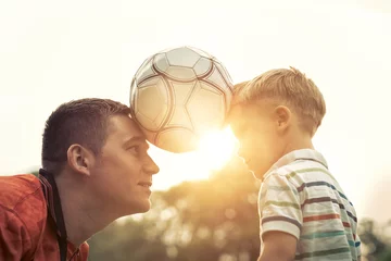 Fototapeten Father and son playing football in park at sunny day © Andrii IURLOV