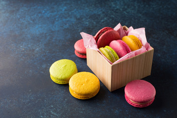 Colorful macaroons gift box. Sweet macarons present on blue table with copy space. Selective focus. Holiday time concept