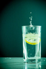 Glass glass of water with lemon on the isolated background. Mountain ineralnaya pure mountain water with gas bubbles and a lemon slice and spray tonic refreshing sports drink.
