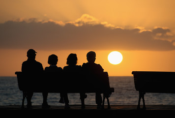 Fototapeta na wymiar Silhouette of a group of seniors who sits on the bench, looking at the sunset