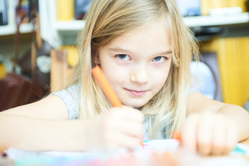 Funny little child girl is drawing and painting with colorful felt-tip pens. Preschooler girl creating at home sitting at table.