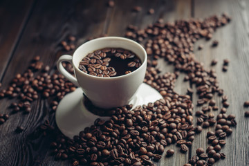 a cup of coffee on an inverted saucer with disheveled coffee beans