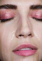 Seductive blonde with beautiful make-up. Pink shade, beauty portrait of a sexy girl. A tender girl. Beautiful girl with a gentle make-up. The girl transparent liquid dripping down his face.