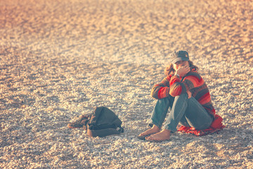 Woman in a cap with a backpack sitting on the pebble beach