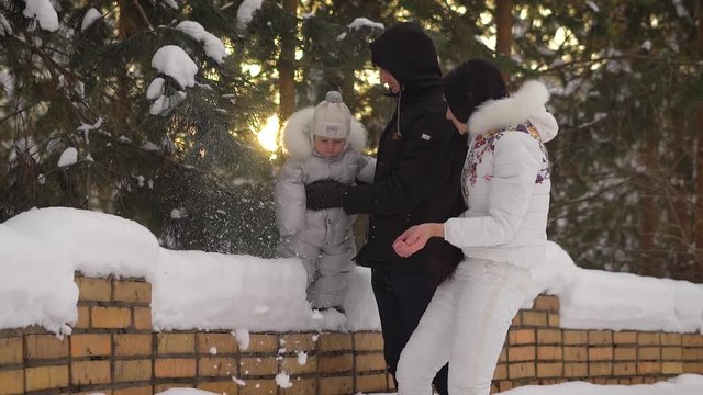 Young mother trying to cheer up his little child, who is backed by the pope, To the fell. Woman throws snow up, and then the snow flies away to the side. Happy family spending time in winter park with