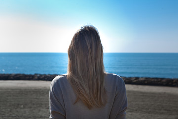 Fototapeta na wymiar donna seduta di spalle sugli scogli guarda il mare