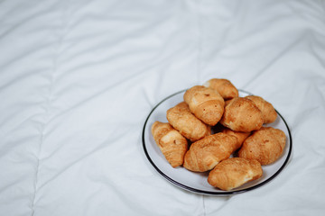 Golden yellow brown yellow tasty delicious sweet croissants, white plate with black stripe in a white bed in the front right foreground with blankets white background