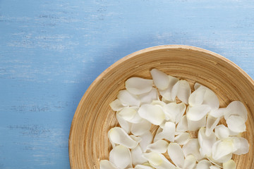 Petals of white roses on blue painted rustic background. Fresh natural flowers in bowl. Dirty grunge wooden board.