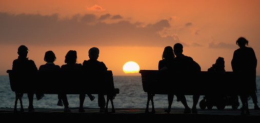 Silhouette of a group of people who sits on the bench, looking at the sunset