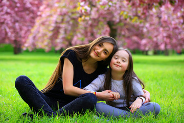Happy beautiful young woman with girl in blossom park with trees and flowers.