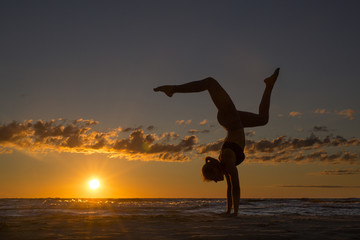 Fototapeta na wymiar Harmonious landscape with a woman practicing yoga upside-down by the sea at sunset.